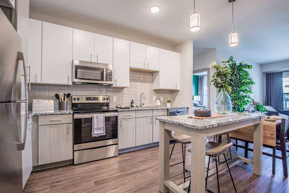 A modern kitchen with a stainless steel refrigerator, oven, and wooden flooring.