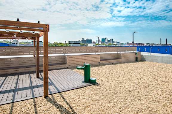 A sandy beach area with a wooden pergola and a green trash can.