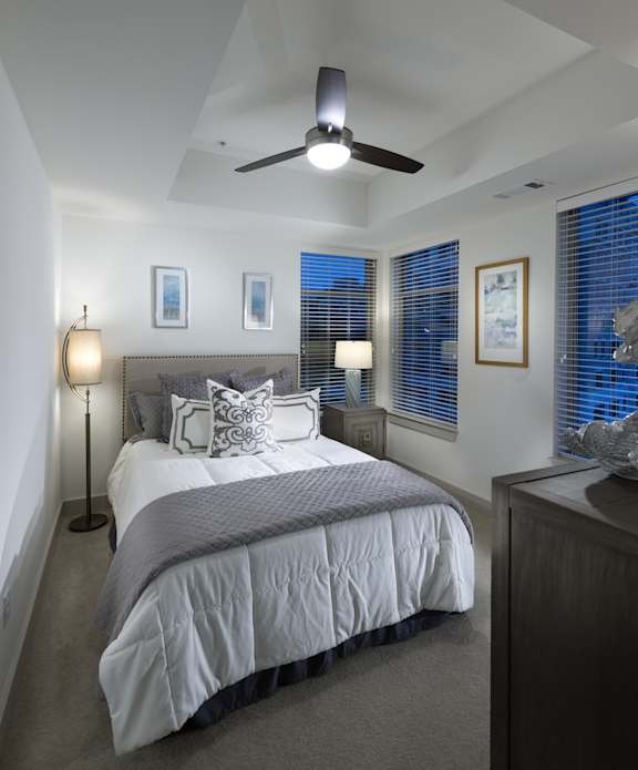 A bedroom with a bed, a ceiling fan, and a nightstand with a lamp.