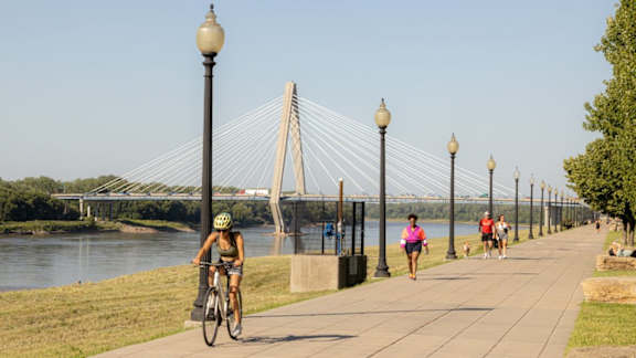 A woman rides her bike on a path next to a river.