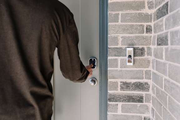 A person in a brown shirt is opening a door with a keypad.