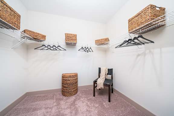 A room with a chair, a basket, and clothes hanging on a rack.