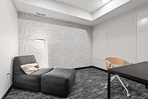 A grey couch with a pillow sits in front of a wallpapered wall.