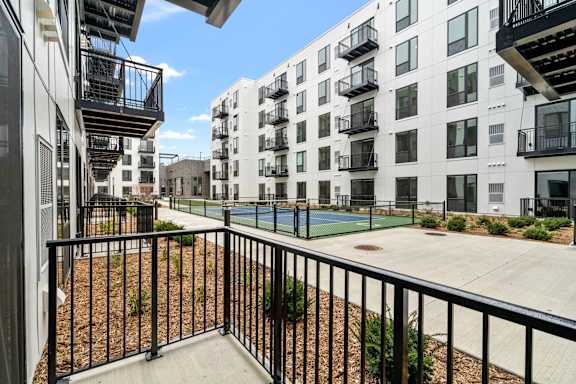 A view of a balcony with a black railing and a tennis court in the background.