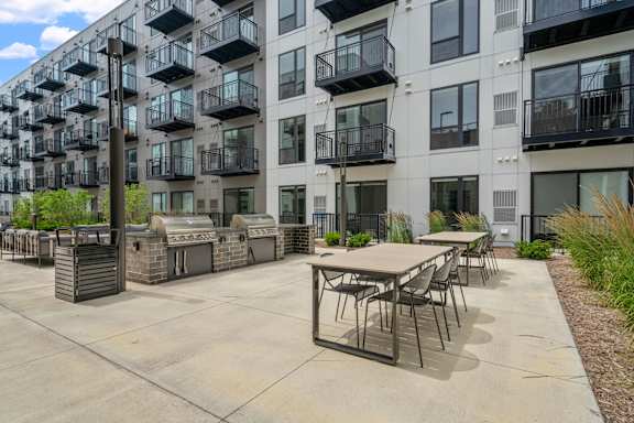 A patio area with tables and chairs is surrounded by apartment buildings.