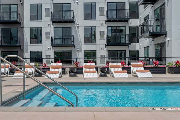 A pool with chairs and a building in the background.