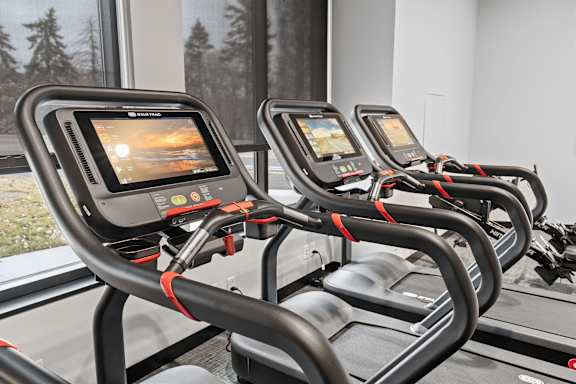 A row of treadmills with screens on the back of the seat.