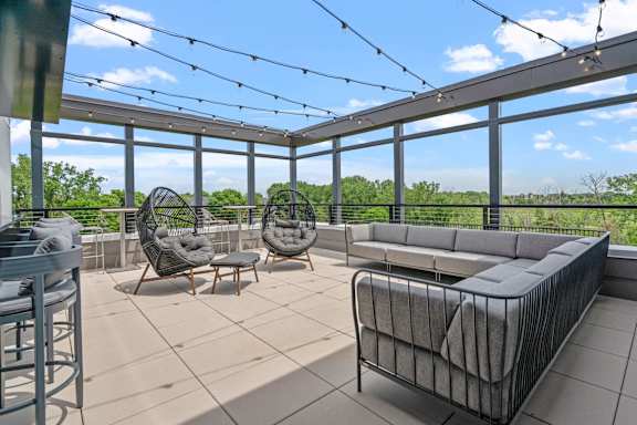 A patio with a grey couch, two chairs and a table.