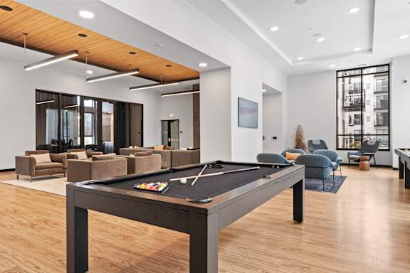 A pool table is in the middle of a room with a woman sitting on a chair.
