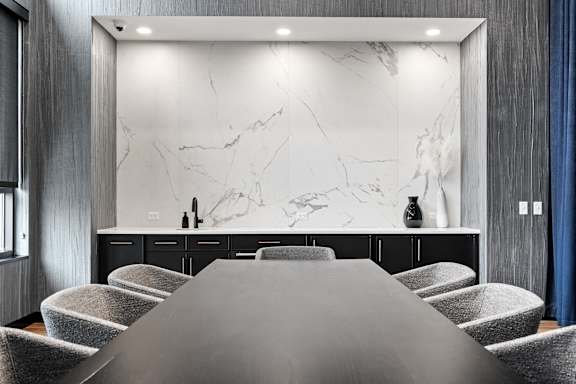 A modern dining room with a marble backdrop and grey chairs.