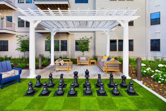 A white pergola is over a lawn with chess pieces on it.