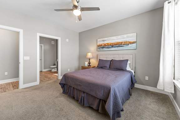 A bedroom with a bed, a ceiling fan, and a painting on the wall.