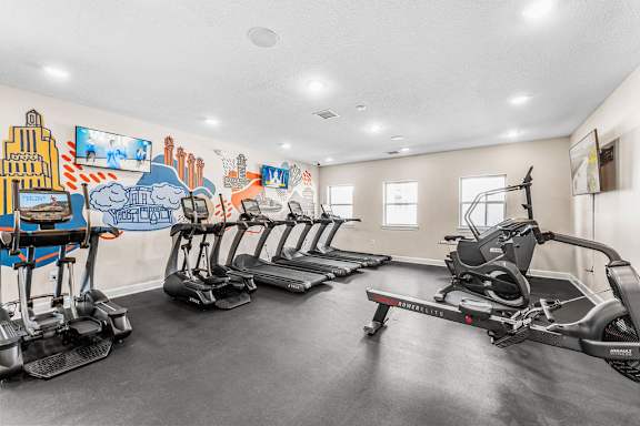 A gym with exercise equipment and a mural on the wall.