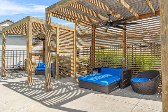 A wooden pergola with a ceiling fan and a blue mattress is in the foreground.
