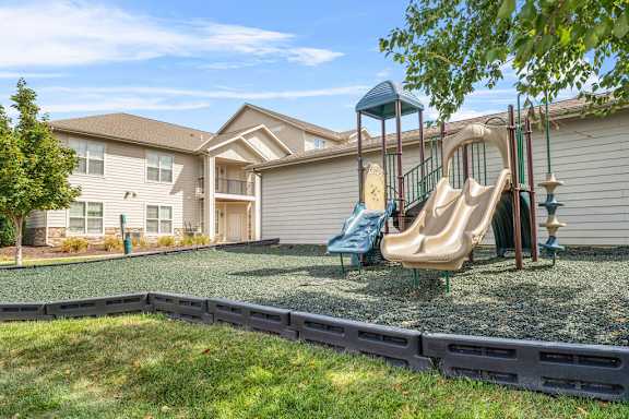 A playground with a slide and a swing set in front of a house.