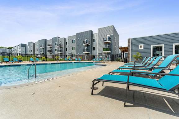 A pool with sun loungers and apartment buildings in the background.