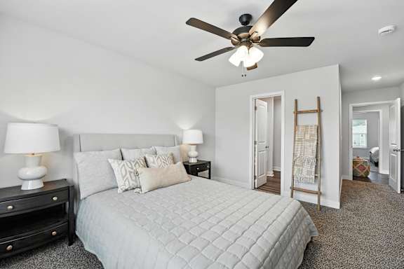 A bedroom with a bed, two lamps, and a ceiling fan.