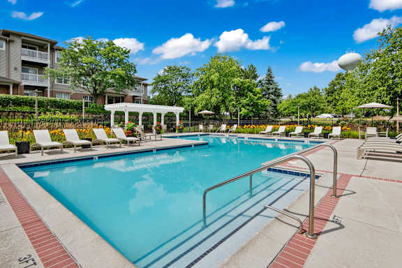 A swimming pool with a red and white striped edge and a white pergola in the background.