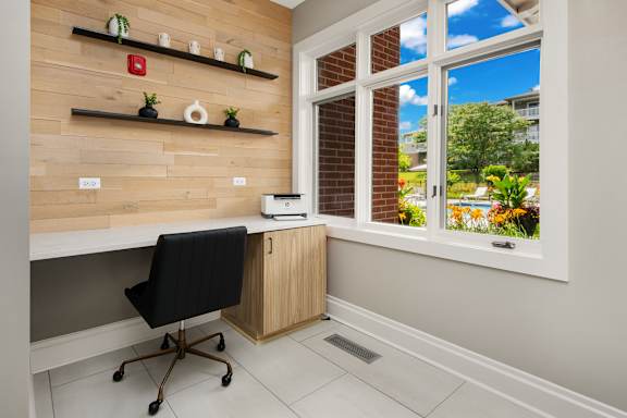 A black chair is in front of a desk with a printer on it.