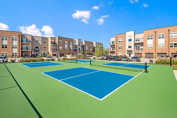 A tennis court is surrounded by apartment buildings.