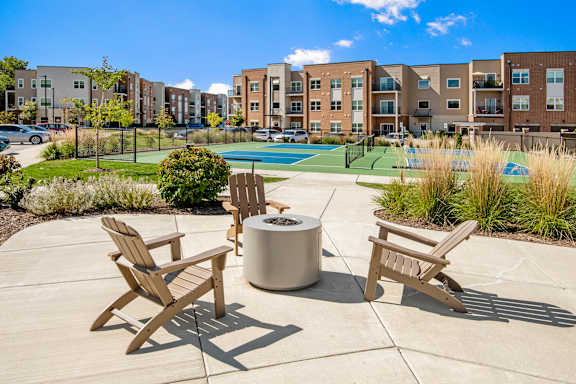 A sunny day at a poolside with chairs and a fire pit.