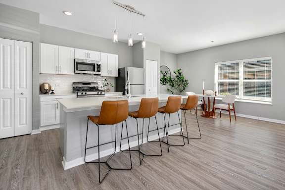 A kitchen with a white countertop and brown chairs.