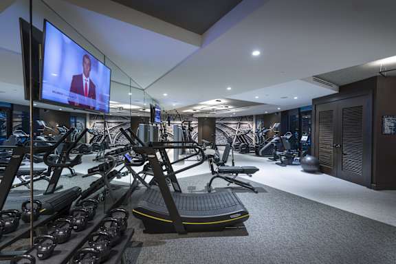 A gym with treadmills and a television screen showing a man in a suit.