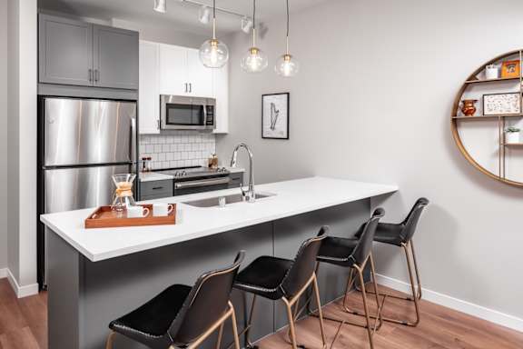 A modern kitchen with a white countertop and black chairs.