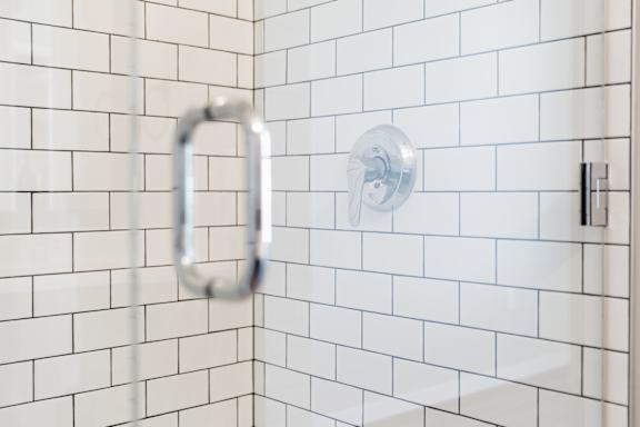 A white tiled shower with a silver faucet.