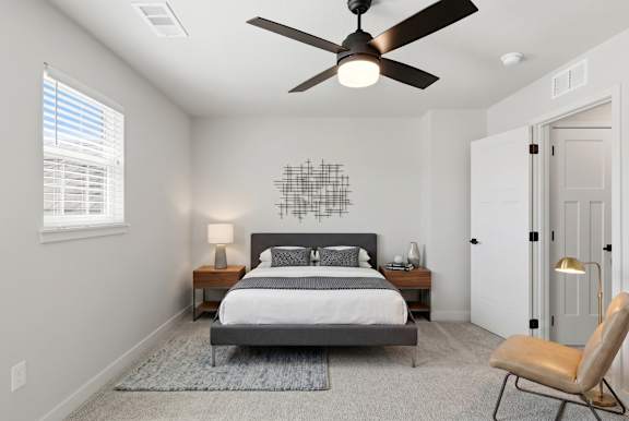 A bedroom with a bed, chair, and ceiling fan.