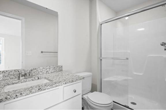 A white bathroom with a marble countertop and a walk-in shower.