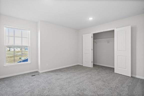 A room with a grey carpet and a window showing a view of a street.