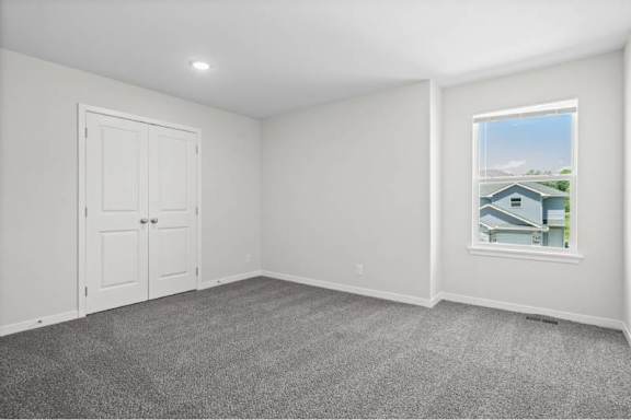 A room with a grey carpet and a window showing a house.