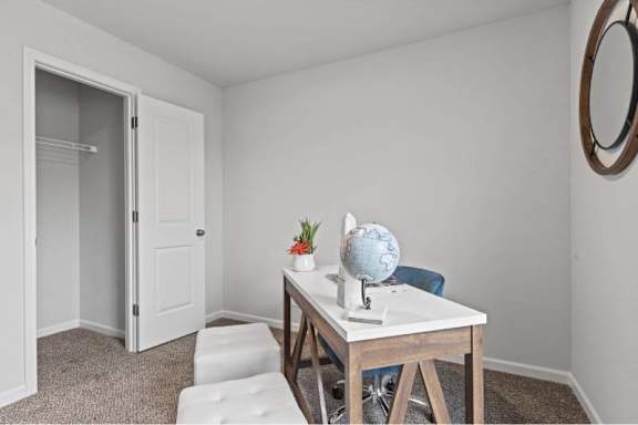 A room with a white door, a table with a globe and a vase with flowers, and a round mirror on the wall.