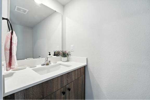 A bathroom with a white countertop and a pink towel hanging on the hook.