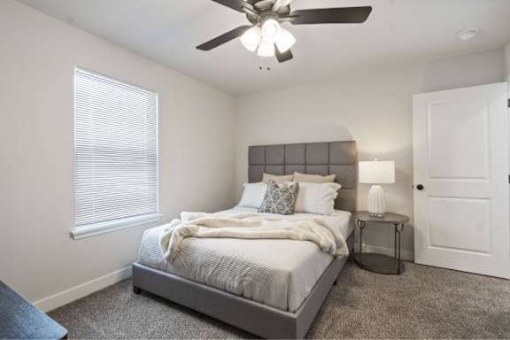 A bedroom with a bed, a ceiling fan, and a nightstand.
