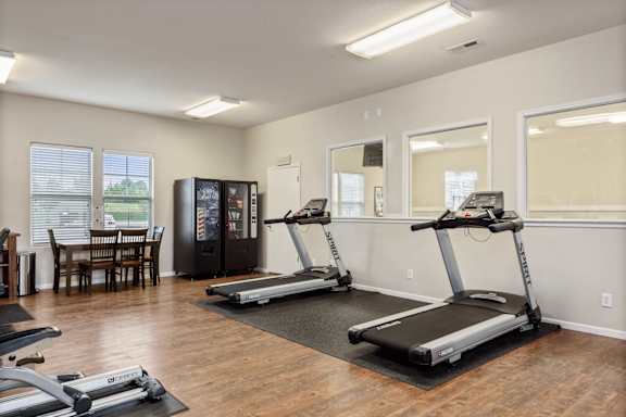 A room with a treadmill, a refrigerator, and a dining table.