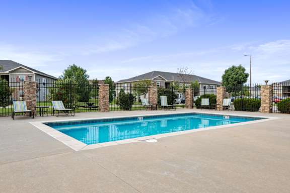 A swimming pool surrounded by a black fence and lawn chairs.