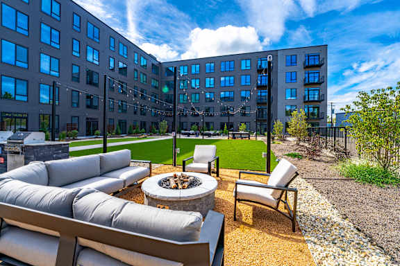A modern outdoor seating area with a fire pit in front of a large building.
