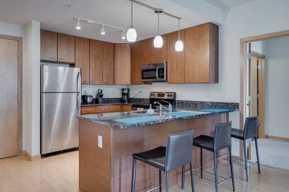 a kitchen with stainless steel appliances and a bar with three chairs at Verge Apartments in St. Louis Park, MN