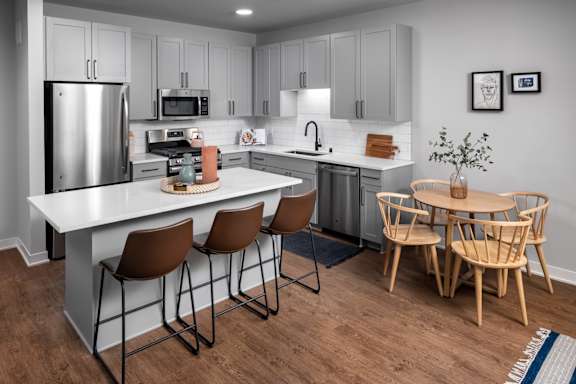 A modern kitchen with a white island and wooden chairs.