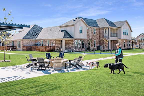 A woman walking a black dog in front of a large brick building.