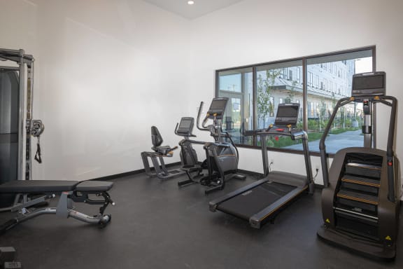 a gym with various cardio equipment on the floor and a window
