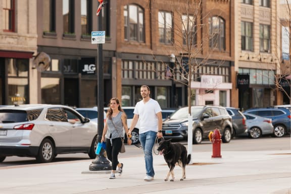 A man and a woman walking a dog down a city street at Mercantile on Broadway, Fargo, ND 58102