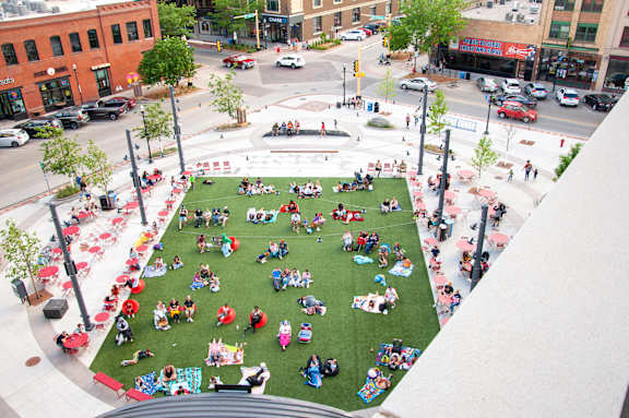 A large group of people are sitting on a grassy area in the middle of a city square at Kesler Apartments in Downtown Fargo, Fargo, North Dakota 58102