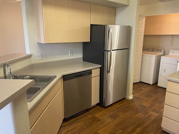 A kitchen with a black refrigerator, white dishwasher, and a washing machine.