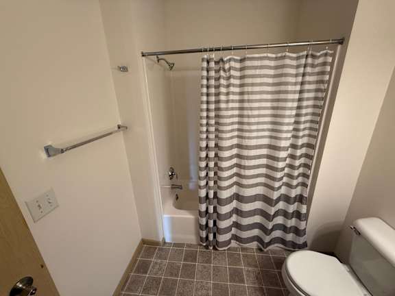 A bathroom with a toilet, a shower curtain, and a tiled floor.