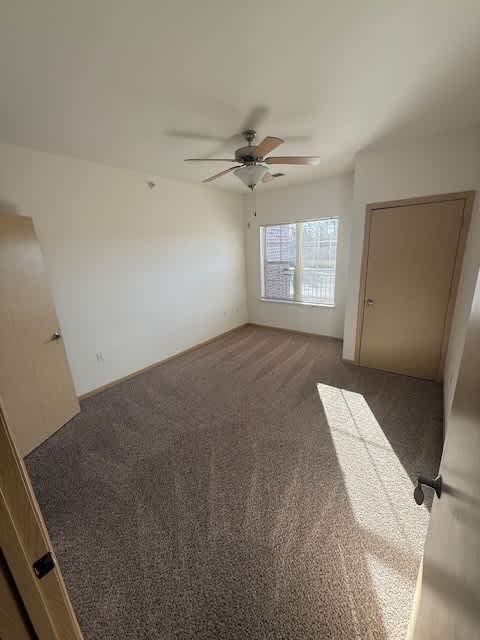 A room with a ceiling fan and carpeted floor.