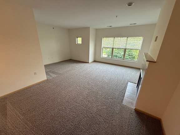 A large, empty room with a carpeted floor and a window with blinds.