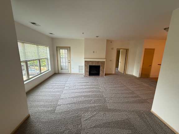 A large, empty room with a fireplace and a carpeted floor.